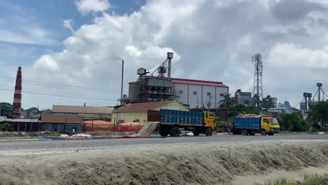 Industrial-factory-with-chimney-and-parked-machines,-drive-by-view