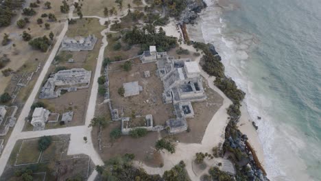 Aerial-rotating-drone-shot-of-the-Mayans-ruins-on-the-beach-of-tulum-with-a-wonderful-view-of-the-sea-and-the-landscape-with-trees-and-rocks-on-4k