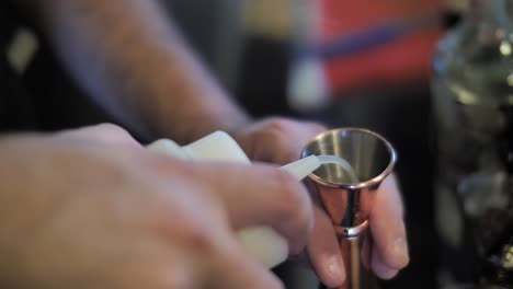 Pouring-syrup-into-metal-measure-glass-while-prepare-cocktail,-close-up