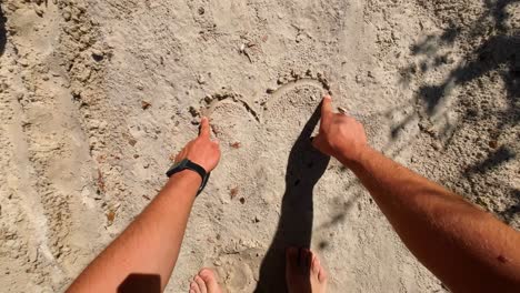 pov-shot-of-man-drawing-a-heart-on-the-sand