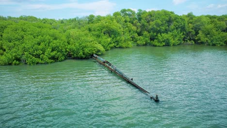 Aerial-shot-of-rusty-leaking-pipe-running-into-lake-surrounded-by-mangroves,-dumping-sewage