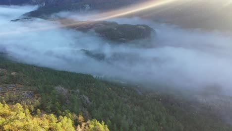 Morning-haze-filling-bottom-of-Eksingedalen-valley-while-first-sun-rays-penetrating-through-top-frame--Downward-moving-aerial-towards-road-in-bottom-of-valley---Norway