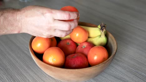 Person-Taking-Clementine-From-Fruits-Bowl-Placed-On-Wooden-Table,-Nested-Sequence