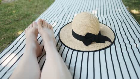Female-feet-and-summer-straw-hat-placed-on-striped-mattress-on-the-ground-in-shade