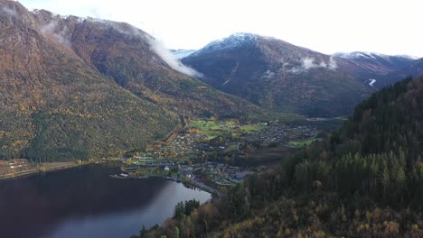 Town-of-Kinsarvik-disappearing-behind-lush-autumn-hillside---Backward-moving-aerial-from-Hardanger-Norway