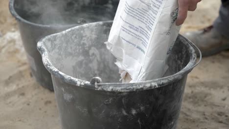 Pouring-A-Bag-Of-Lime-Mortar-Into-Bucket-For-Mixing
