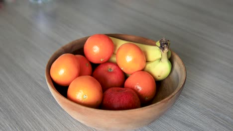 Persona-Que-Elige-Manzana-Fresca-De-Un-Tazón-De-Frutas-Colocado-En-Una-Mesa-De-Madera,-Secuencia-Anidada