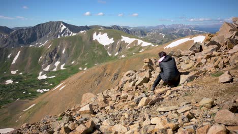 Female-photographer-sitting-on-edge-of-slope-taking-picture-of-Colorado-Rocky-Mountains-during-the-winter,-handheld