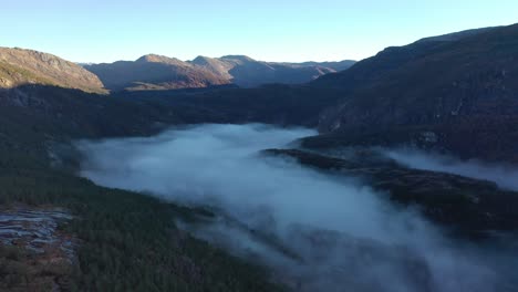 Neblina-Matutina-Llenando-El-Fondo-Del-Valle-De-Eksingedalen-En-Noruega-Durante-El-Amanecer-Temprano-En-La-Mañana-Entre-Montañas---Antena-En-Movimiento-Hacia-Arriba-En-El-Paisaje-Salvaje-Y-El-Bosque