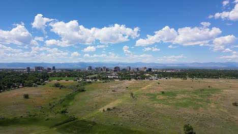 Flying-Over-The-Green-Meadow-With-High-rise-Buildings-In-The-Distance-In-Denver-City,-Colorado,-USA