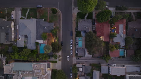 Aerial-Drone-Shot-of-White-Car-Making-U-Turn-in-Middle-of-Intersection-in-Residential-Suburban-Neighborhood,-Palm-Trees-and-Pools-Seen-from-Above