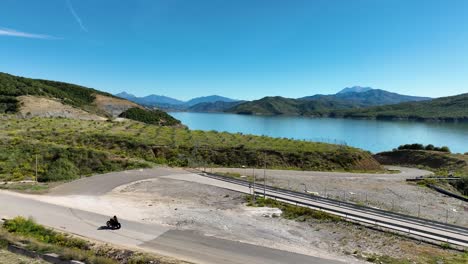 Motociclista-Viajando-Por-La-Carretera-Rural-Del-Pueblo-Supervisando-El-Lago-Azul-Y-Las-Montañas