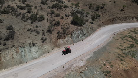 Dron-Siguiendo-A-Un-Camionero-Rojo-Conduciendo-Lentamente-Por-Una-Carretera-En-Turquía-Karaman-Entre-Campos-Y-Montañas-En-Un-Verano-Soleado