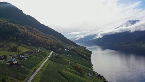 Road-between-Eidfjord-and-Odda-along-Sorfjorden-past-Kinsarvik-in-Hardanger-Norway---Stunning-landscape-with-fruit-farms-to-the-left-and-snow-capped-mountain-peaks-on-right---Autumn-aerial-Norway