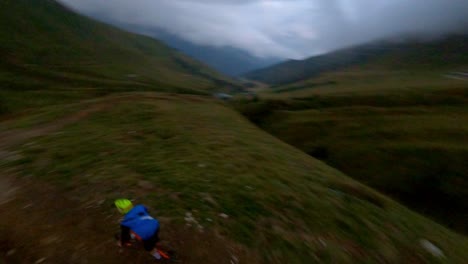 Extreme-mtb-cyclist-speeding-down-mountain-trail-into-valley-during-cloudy-day---aerial-fpv-tracking-shot