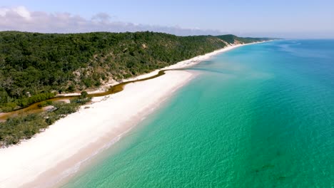 Aerial-view-of-Fraser-Island,-the-beautiful-beach-and-aqua-toned-water-is-being-revealed-with-a-slow-drone-pan-up-on-a-sunny-day