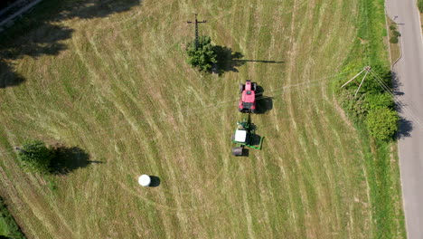 Agriculture-Machinery-in-Green-Field,-Tractor-and-Hay-Bales-Machine-Rotating-in-Agricultural-Farmland,-Aerial-Top-Down-View-of-Farm-Agricultural-Work