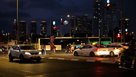 Stopped-cars-at-red-light-in-busy-intersection-and-pedestrian-crossing-in-large-city-at-night,-Tel-Aviv-Israel