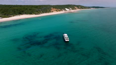 Aerial-footage-of-a-tourist-boat-anchored-on-the-shores-of-Fraser-Island,-the-slow-pan-up-reveals-the-island-behind-the-vessel
