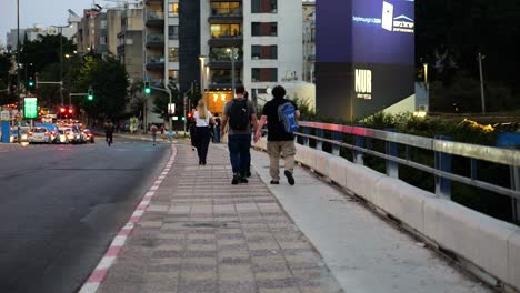 People-walking-down-the-bridge-on-pedestrian-sidewalk-by-a-busy-road,-Tel-Aviv-Israel