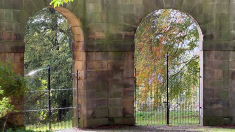 Old-stone-arches-with-iron-gates-and-the-sunlight-shining-through-them-and-golden-autumn-trees-in-the-distance
