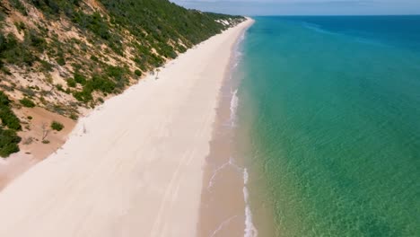 Slow-drone-pan-up-reveals-the-beautiful-beaches-around-Fraser-Island-surrounded-by-aqua-toned-water-and-colorful-sand-dunes-on-a-sunny-day