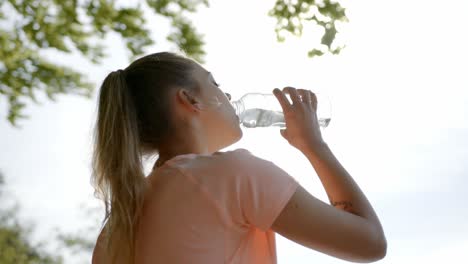 Woman-standing-under-tree-drinking-water-from-bottle