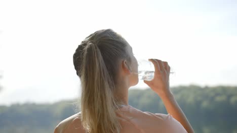 Mujer-Bebiendo-Agua-De-Una-Botella-Frente-Al-Lago