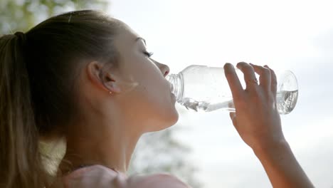 Mujer-Parada-Frente-Al-Lago-Bebiendo-Agua-De-Una-Botella