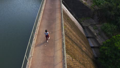 Shot-from-a-drone-of-a-woman-walking-on-the-top-of-a-dam-and-look-at-the-reservoir-during-the-day