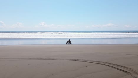 Man-riding-a-scooter-along-a-long-empty-beach-in-central-America