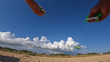 Low-angle-pov-of-male-hands-controlling-flying-green-kite-over-sandy-beach-by-holding-green-handles