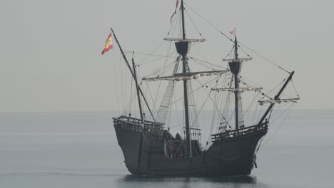 Ferdinand-Magellan-Nao-Victoria-carrack-boat-replica-with-spanish-flag-sails-in-the-mediterranean-at-sunrise-in-calm-sea-side-shot-in-slow-motion-60fps