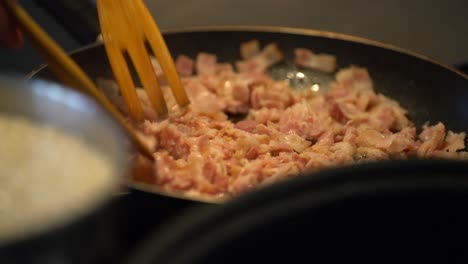 Mixing-raw-thin-diced-bacon-in-pan-with-forked-wooden-spoon