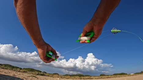 First-person-view-of-male-hands-controlling-flying-green-kite-with-long-tail-over-sandy-beach-by-holding-green-handles