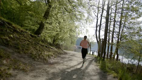 Runner-running-through-trees-in-woods-near-lake-on-sunny-day