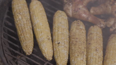 Smoking-corn-on-a-cob-and-barbecue-chicken-legs-on-a-charcoal-black-kettle-grill-at-a-public-park-in-summer
