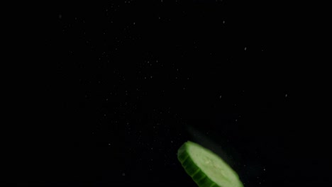 Cucumber-slice-falling-into-water-on-front-of-the-black-screen
