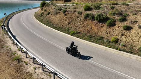 Biker-adjusting-visor-while-riding-on-a-coutry-road-overseeing-blue-lake