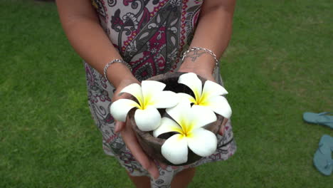 Woman-is-standing-on-the-grass-and-she-keeps-on-her-hands-a-cap-with-white-Plumeria-Hawaiian-flowers,-picked-up-in-the-morning