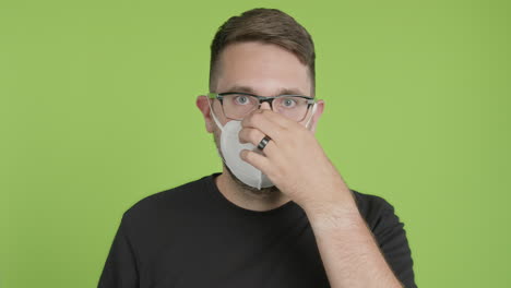 Man-in-Glasses-Puts-on-Protective-KN95-Face-Mask-While-Looking-Into-Camera-on-Green-Screen-Chroma-Key
