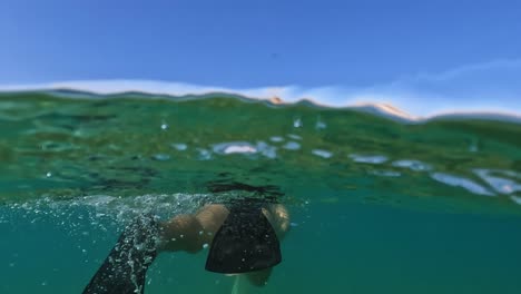 Half-underwater-rear-view-of-adult-man-with-mask-and-yellow-snorkel-swimming-in-blue-Adriatic-sea-with-diving-fins-along-trabocchi-fishing-platforms-in-Abruzzo,-Italy