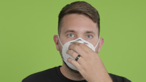 Man-Puts-on-Protective-KN95-Face-Mask-While-Looking-Into-Camera-on-Green-Screen-Chroma-Key-Close-Up