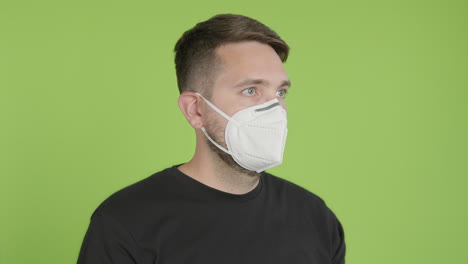 Man-Puts-on-Protective-KN95-Face-Mask-While-Looking-Right-of-Camera-on-Green-Screen-Chroma-Key