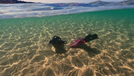Ungewöhnliche-Geteilte-Unterwasseransicht-Von-Verlorenen-Fuchsiafarbenen-Taucherflossen,-Die-Auf-Dem-Meeresboden-Ruhen
