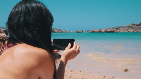 A-woman-playing-with-her-smartphone-laying-on-the-beach
