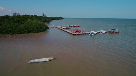 Boat-dock-in-lagoon-on-island-Holbox-in-Mexico,-tourists-on-wooden-dock,-parked-boats,-aerial-flyover