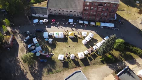 top-view-of-small-colorful-tents-in-a-farmers-market-next-to-a-red-brick-factory-building-in-a-warm-sunny-day