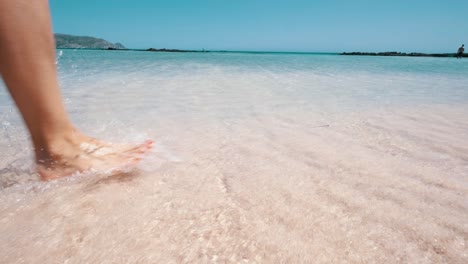 Girl-walking-on-the-pink-beach,-feet-in-water