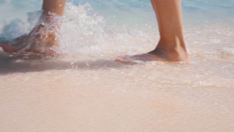 Girl-walking-on-the-pink-beach,-feet-in-the-sea